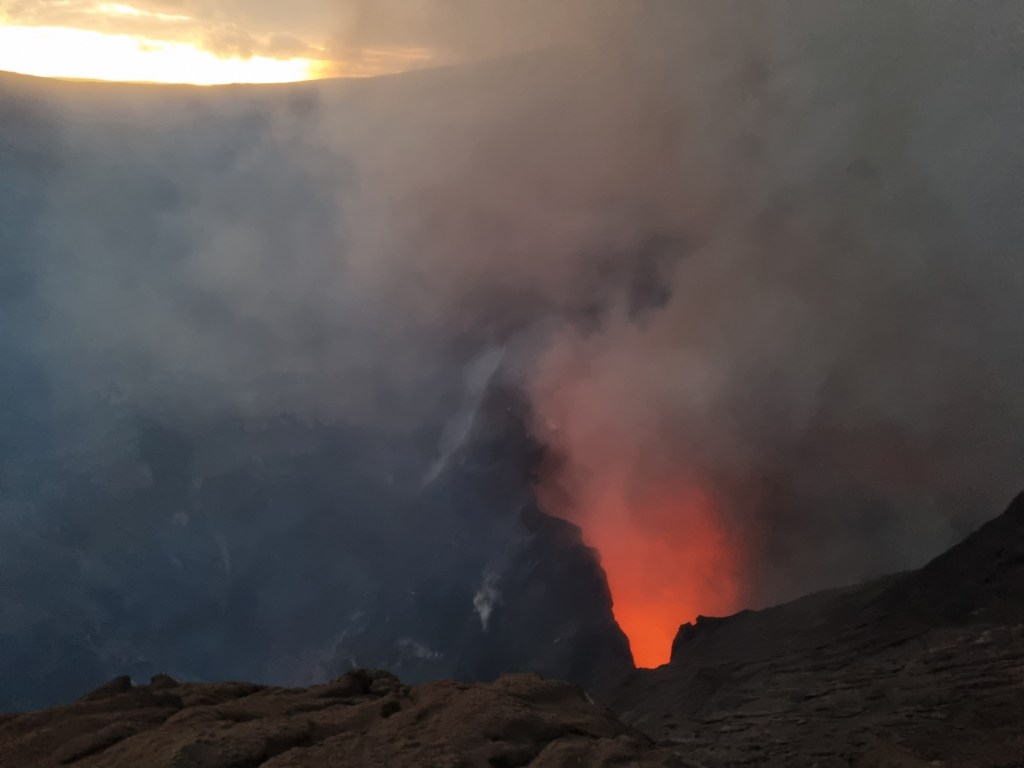 A volcanic crater glowing orange with smoke spewing from it.